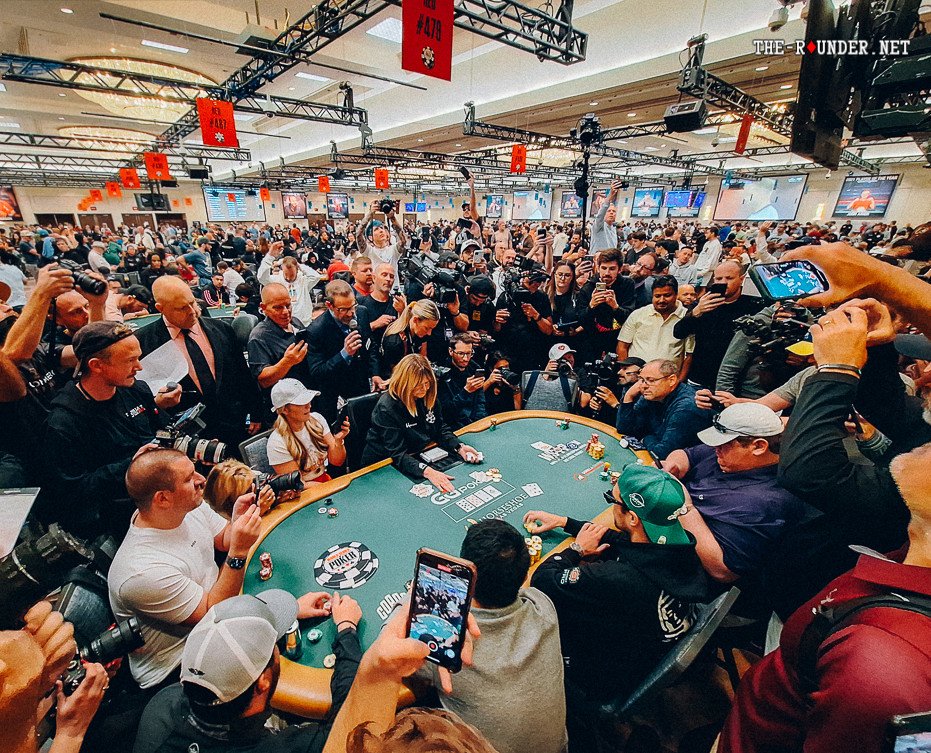 Ein professioneller Pokertisch mit grünem Filz und Chips auf dem Tisch, umgeben von vier Spielern, die Karten halten und konzentriert aussehen.