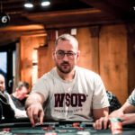 Ein professioneller Pokertisch mit grünem Filz, umgeben von Stühlen und Chips. In der Mitte des Tisches liegen Spielkarten und ein Stapel Jetons. Im Hintergrund sind unscharfe Sil