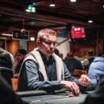 Ein professioneller Pokertisch mit grünem Filz und einem Stapel von Pokerchips. In der Mitte des Tisches liegen Spielkarten und Spieler sind beim Pokerspiel engagiert.