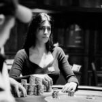 Ein Mann sitzt an einem Pokertisch und hält Karten in der Hand, während er konzentriert auf seine Gegner schaut.