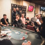 Ein professioneller Pokertisch mit grünem Filz und Pokerchips in verschiedenen Farben, umgeben von Spielern, die ihre Karten halten und konzentriert auf ihre Hände schauen.