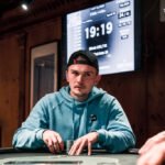 Ein Mann und eine Frau sitzen an einem Pokertisch und spielen eine Partie Poker. Der Mann hat Karten in der Hand und schaut konzentriert auf den Tisch, während die Frau mit gespanntem Blick ihre eigenen