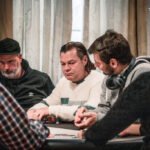 Ein Mann und eine Frau sitzen an einem Pokertisch und spielen Texas Hold'em. Der Mann hat eine große Hand voll Pokerchips, während die Frau konzentriert ihre Karten betrachtet. Im Hintergrund sind weitere Spieler