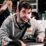 Ein Mann und eine Frau sitzen an einem Pokertisch in einem eleganten Casino. Der Mann hat einen Anzug an und hält Pokerkarten in der Hand, während die Frau konzentriert auf ihre Karten schaut. Im
