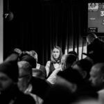 Ein Mann und eine Frau sitzen lächelnd an einem Pokertisch und spielen Karten. Die Frau hält Karten in der Hand, während der Mann seine Chips stapelt. Im Hintergrund sind Pokerchips und Getr