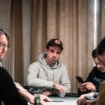 Ein Mann und eine Frau spielen Poker an einem eleganten Tisch mit grüner Filzdecke. Die Frau hält Karten in der Hand und schaut konzentriert auf ihre Chips, während der Mann mit ernstem Gesicht