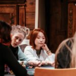 Ein buntes und lebendiges Pokerspiel mit mehreren Personen an einem Tisch, die Karten halten und konzentriert auf ihre Hände schauen. In der Mitte des Tisches liegen Pokerchips und Spiel