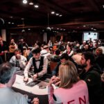 Ein professioneller Pokertisch mit grünem Filz und Pokerchips in verschiedenen Farben, umgeben von vier Spielern, die konzentriert ihre Karten betrachten und ihre Einsätze platzieren.