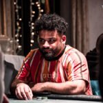 Ein Mann und eine Frau sitzen an einem Pokertisch und spielen eine Partie Poker. Der Mann hat eine Hand mit Spielkarten in der Hand und schaut konzentriert auf seine Karten, während die Frau mit ernstem Ges