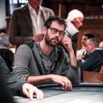 Ein buntes Pokerspiel mit Spielkarten, Pokerchips und Getränken auf einem Tisch in einem gemütlichen Wohnzimmer.