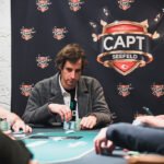 Ein Mann spielt Poker an einem Tisch in einem Casino, umgeben von anderen Spielern und einem Dealer.