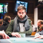 Ein Bild von vier Personen, die an einem Pokertisch sitzen und Karten spielen. Die Personen sind konzentriert und haben Pokerchips vor sich liegen. Ein Spieler hat gerade seine Karten aufgedeckt.