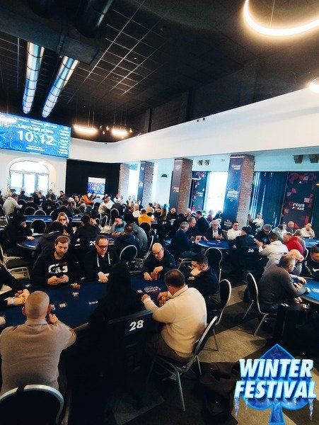 Ein fröhliches Paar sitzt an einem Tisch und spielt Poker. Der Mann hat eine Hand mit Karten in der Luft, während die Frau konzentriert ihre Karten betrachtet. Im Hintergrund sind Pokerch