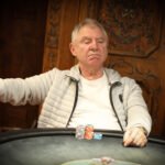 Ein Mann sitzt an einem Pokertisch und hält Karten in der Hand, während er konzentriert auf das Spiel schaut. Um ihn herum sind Chips und Getränke zu sehen.