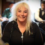 Ein professioneller Pokerspieler sitzt an einem Tisch, umgeben von Chips und Karten. Er betrachtet konzentriert seine Hand und hat einen ernsten Gesichtsausdruck.