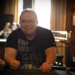 Ein Mann und eine Frau sitzen an einem Pokertisch und spielen Karten. Der Mann trägt einen Anzug und die Frau ein elegantes Abendkleid. Die Atmosphäre ist spannungsgeladen und die beiden haben ern