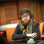 Ein professioneller Pokerspieler mit Sonnenbrille und Kopfhörern konzentriert sich am Tisch auf seine Karten während eines Turniers.