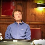 Ein eleganter Pokertisch mit grünem Filz, umgeben von luxuriösen Ledersesseln, Gläsern mit Getränken und einer glänzenden Decke. In der Mitte des Tisches