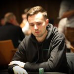 Ein glamouröses Foto von vier Personen, die an einem Pokertisch sitzen und Karten spielen. Die Spieler sind elegant gekleidet und konzentriert, während sie ihre Karten betrachten. Der Tisch ist mit Poker