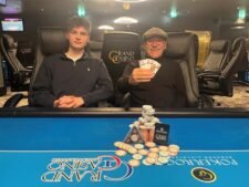 Ein bunter Haufen von Spielkarten auf einem Tisch, umgeben von Chips und Gläsern. Menschen sind im Hintergrund zu sehen, während sie Poker spielen.