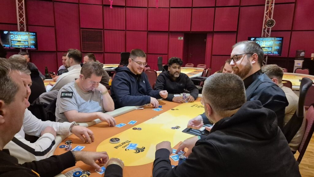 Ein Mann sitzt an einem Pokertisch und hält zwei Karten in der Hand, während er konzentriert auf seine Gegner schaut.