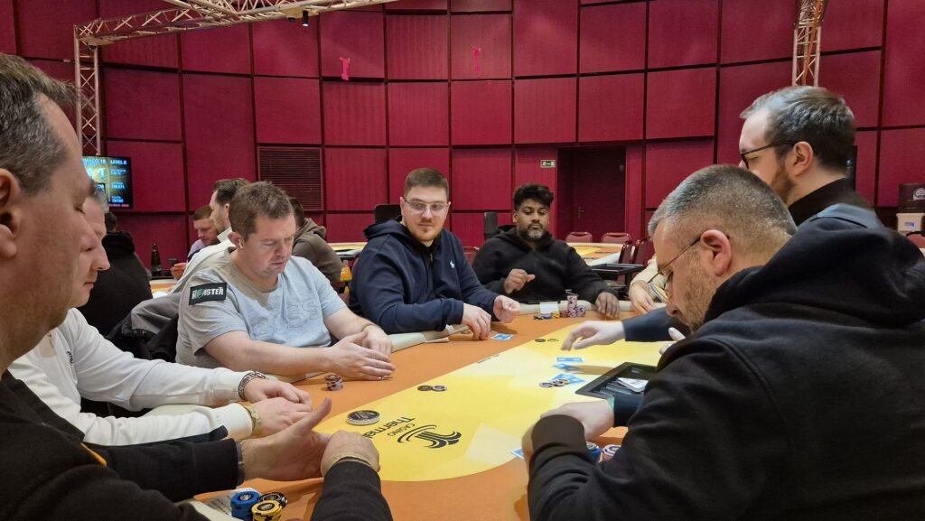 Ein stilllebenartiges Foto einer Pokerrunde mit verschiedenen Spielkarten, Pokerchips und Getränken auf einem Tisch. Es herrscht eine gespannte Atmosphäre, da die Spieler ihre Karten betrachten