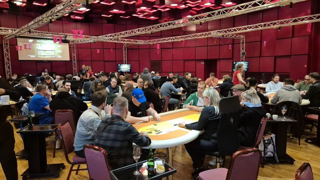 Ein Mann sitzt an einem Pokertisch und hält zwei Könige (König-König) in der Hand. Er hat eine ernste Miene und starrt konzentriert auf seine Karten. Andere