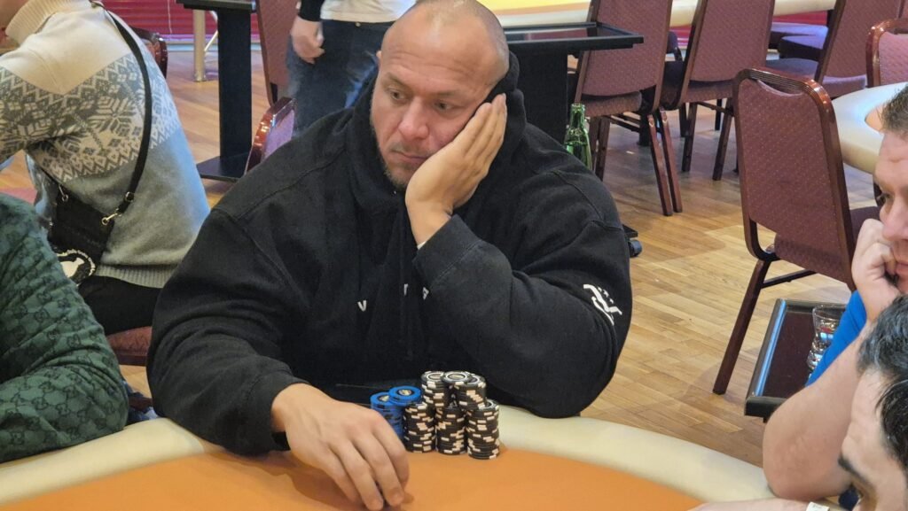 Ein professioneller Pokertisch mit grünem Filz und Chips, Karten und Getränken darauf. Zwei Personen sind dabei, eine Partie Poker zu spielen.