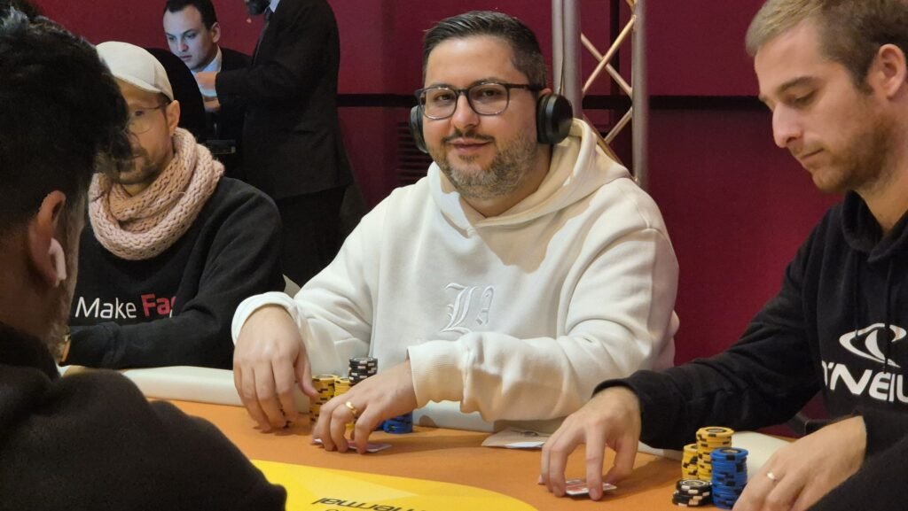 Ein Poker-Tisch mit grüner Filzdecke, umgeben von Spielkarten, Pokerchips und Getränken. Mehrere Personen sitzen um den Tisch und spielen eine Runde Poker.