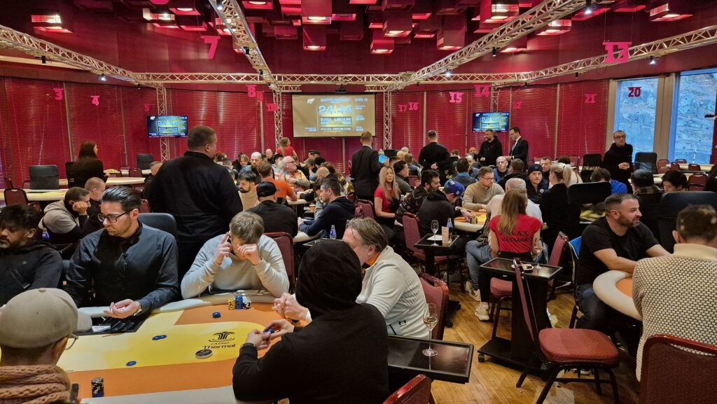 Ein Mann in einem dunklen Anzug und einer schwarzen Sonnenbrille sitzt an einem Pokertisch mit grünem Filz. Er hält seine Karten in der Hand und schaut konzentriert auf den Tisch