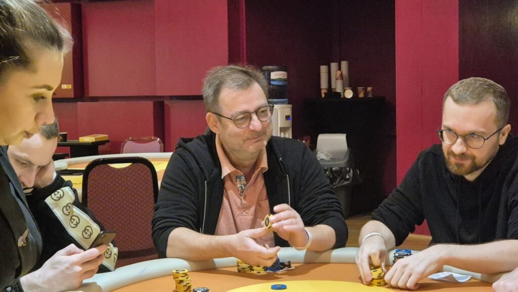 Ein Bild eines Pokertisches mit Spielkarten, Pokerchips und Getränken, umgeben von Spielern in einem Casino.