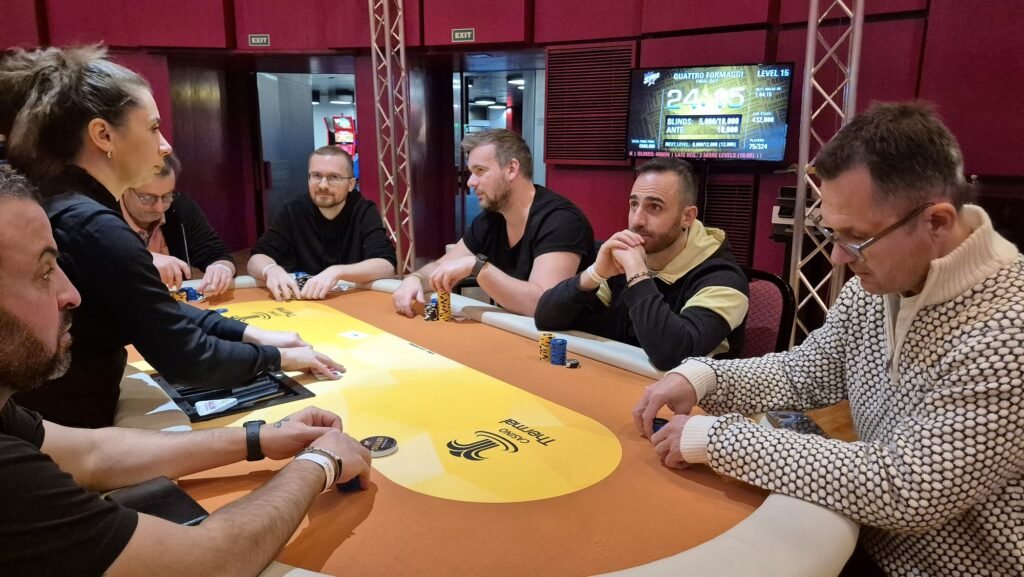 Ein professioneller Pokertisch mit grüner Filzoberfläche, umgeben von mehreren Spielern, die Karten halten und Chips stapeln. Ein Dealer sitzt in der Mitte und mischt die Karten. Die Spieler
