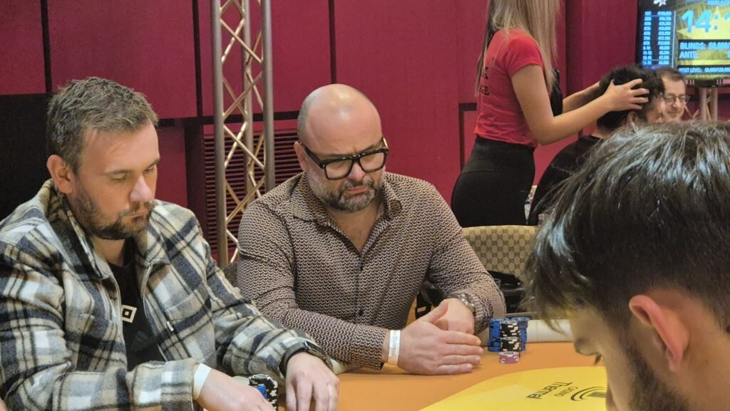 Ein professioneller Pokertisch mit grünem Filz, umgeben von Stühlen und Spielchips, während Spieler ihre Karten halten und setzen.
