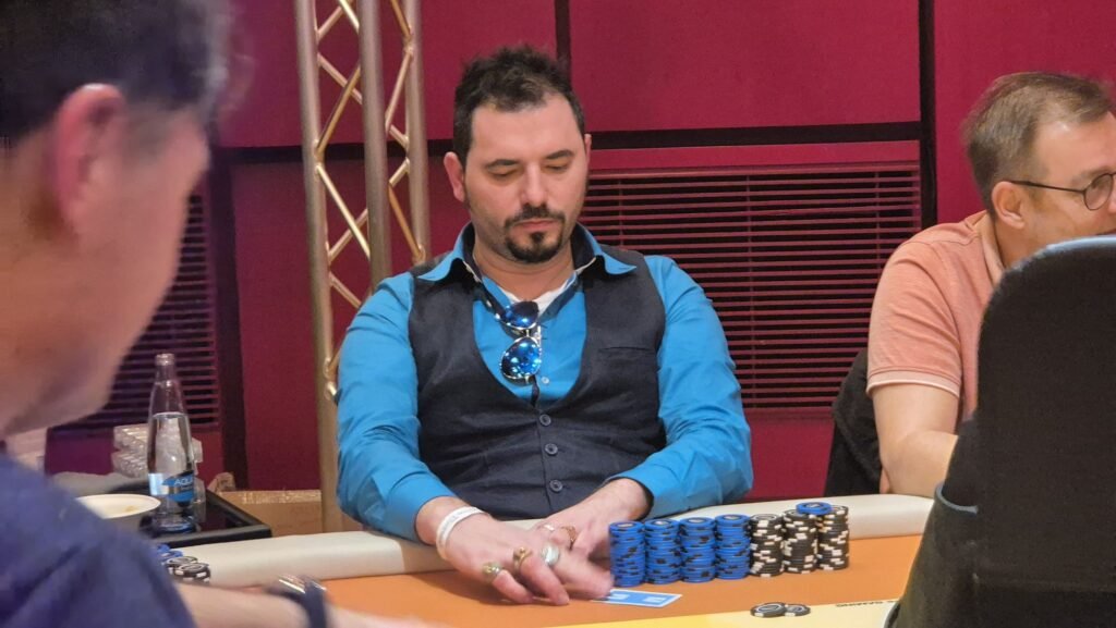 Ein professioneller Pokertisch mit grünem Filz und neun Sitzplätzen, umgeben von Spielkarten, Pokerchips und Getränken. Zwei Spieler sind in einer intensiven Hand, während andere ges