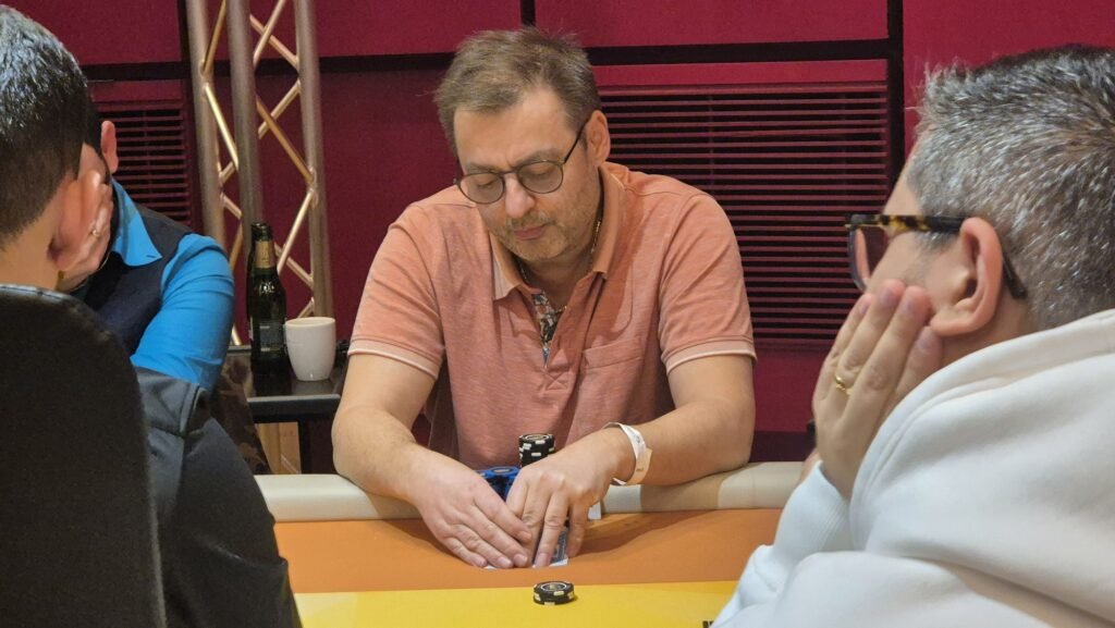 Ein professioneller Pokerspieler mit Sonnenbrille und einem Stapel Pokerchips vor sich sitzt an einem Pokertisch und betrachtet konzentriert seine Karten.