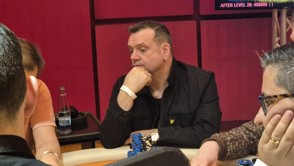 Ein professioneller Pokerspieler mit Sonnenbrille und einem Stapel Pokerchips vor sich, der konzentriert seine Karten betrachtet.