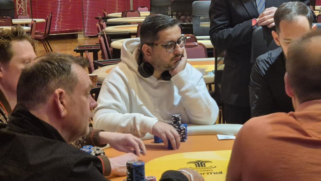 Ein Mann spielt Poker in einem eleganten Kasino, umgeben von anderen Spielern und einer glamourösen Atmosphäre.