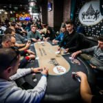 Ein Pokertisch mit grünem Filz, umgeben von Spielern, die Pokerchips stapeln und Karten halten. Ein Spieler in der Mitte des Bildes hat einen Royal Flush mit Ass, König, Dame,