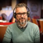 Ein Mann in einem schwarzen Anzug und einer schwarzen Sonnenbrille spielt Poker an einem eleganten Tisch in einem luxuriösen Casino.