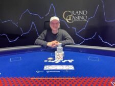 Ein Mann sitzt an einem Pokertisch mit einem großen Stapel Chips vor sich. Er betrachtet konzentriert seine Karten.