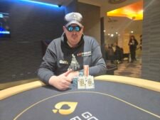 Ein Foto von einem Pokertisch während eines Turniers mit Stapeln von Pokerchips und Spielkarten darauf. Die Spieler sind konzentriert und entschlossen, während sie ihre Hände spielen. Ein Dealer sitzt am Tisch