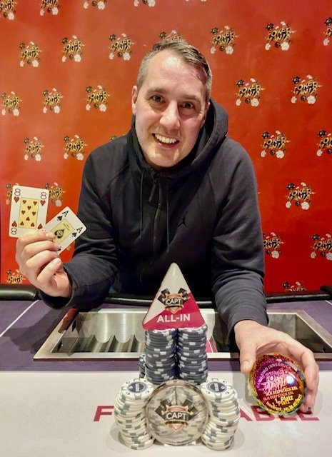 Ein Mann spielt Poker an einem Tisch mit grünem Filz. Er hat einen ernsten Gesichtsausdruck und hält Karten in der Hand. Im Hintergrund sind Pokerchips und eine Getränked