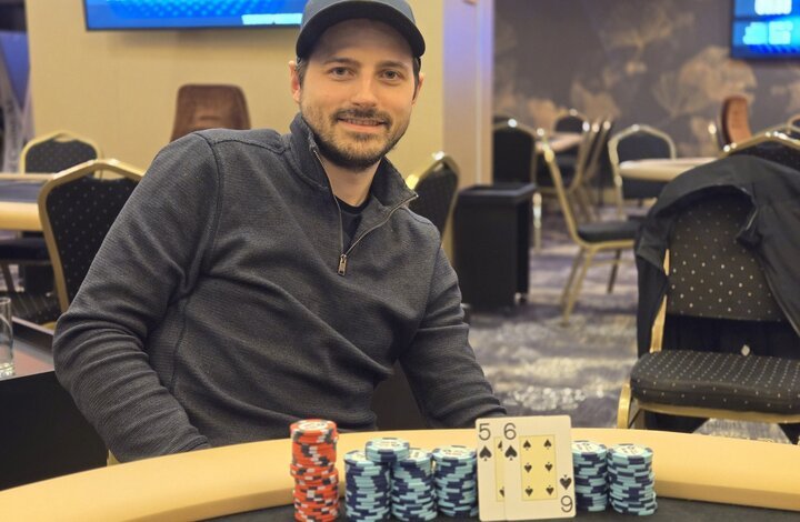 Ein Mann sitzt an einem Pokertisch und hält seine Karten in der Hand, während er konzentriert auf den Spielverlauf schaut. Das Bild zeigt eine spannende Pokerrunde in einem luxuriösen Casino