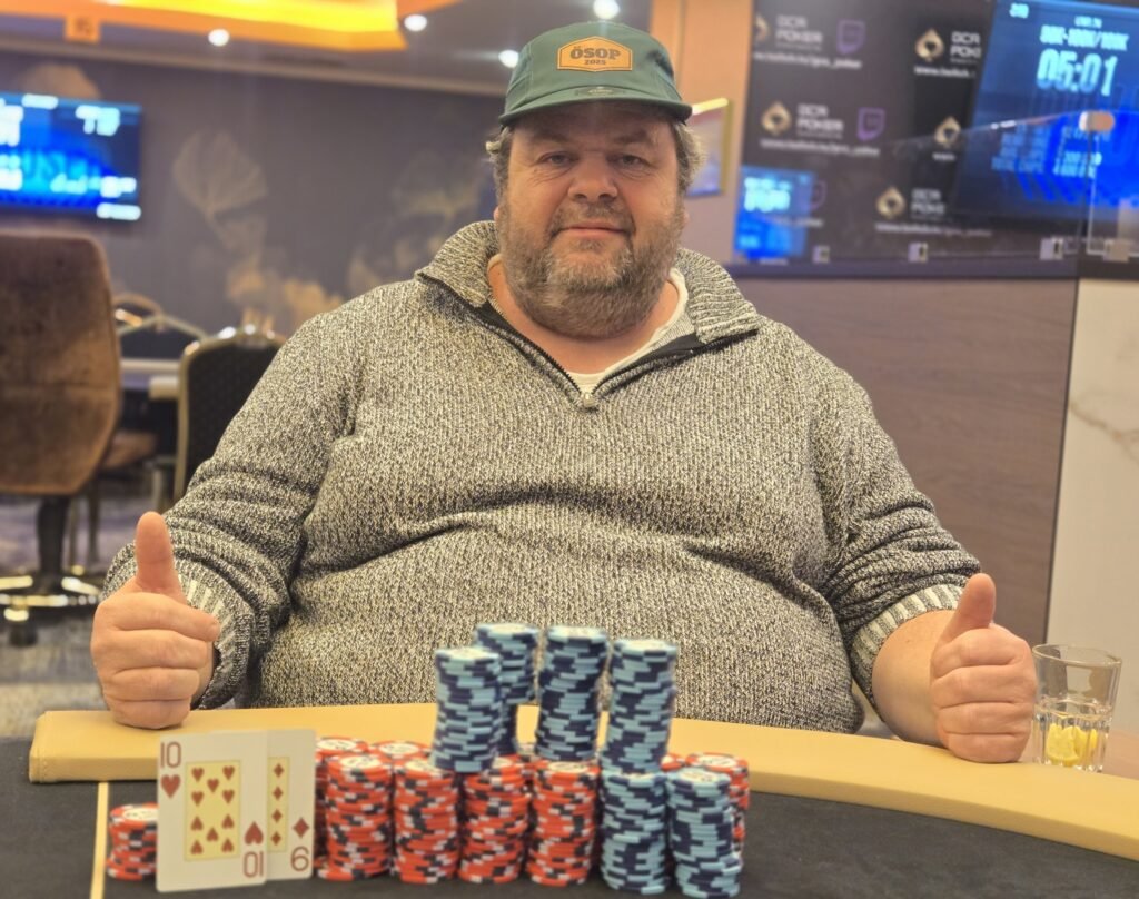 Ein professioneller Pokertisch mit grünem Filz und Pokerchips, Karten und Getränken darauf. Zwei Personen sitzen an dem Tisch und spielen Poker.