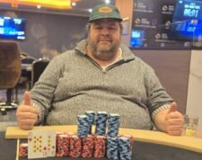 Ein professioneller Pokertisch mit grünem Filz und Pokerchips, Karten und Getränken darauf. Zwei Personen sitzen an dem Tisch und spielen Poker.