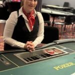 Ein glücklicher Mann hält eine Royal Flush Kartenkombination (Ass, König, Dame, Bube und 10 in Herz) in der Hand während er an einem Pokertisch sitzt.