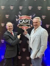 Ein professioneller Pokertisch mit grünem Filz und Chips, umgeben von Spielern, die Karten halten und konzentriert sind.