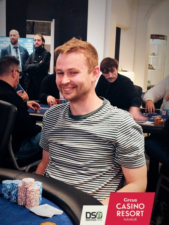 Ein Mann sitzt am Pokertisch, konzentriert und mit gespanntem Gesichtsausdruck. Er hält Karten in der Hand und schaut auf die Mitte des Tisches, wo Pokerchips lie