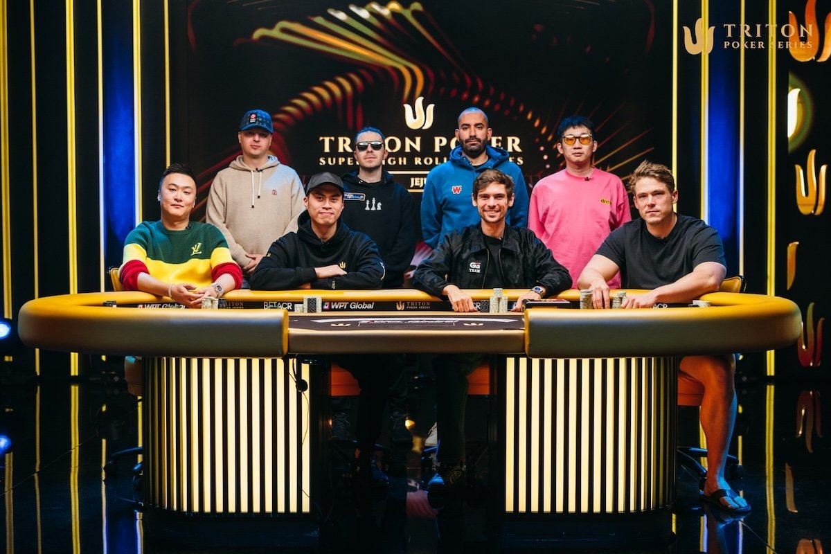 Ein Gruppenfoto von Pokerspielern am Finaltisch des Triton Jeju Event 9, mit Spielern, die Karten halten und Chips stapeln, während sie auf ihre nächsten Züge warten.