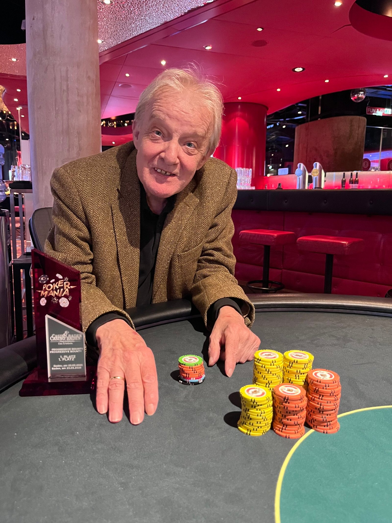 Ein älterer Mann mit grauem Haar und Brille, der konzentriert an einem Pokertisch sitzt und Karten hält.